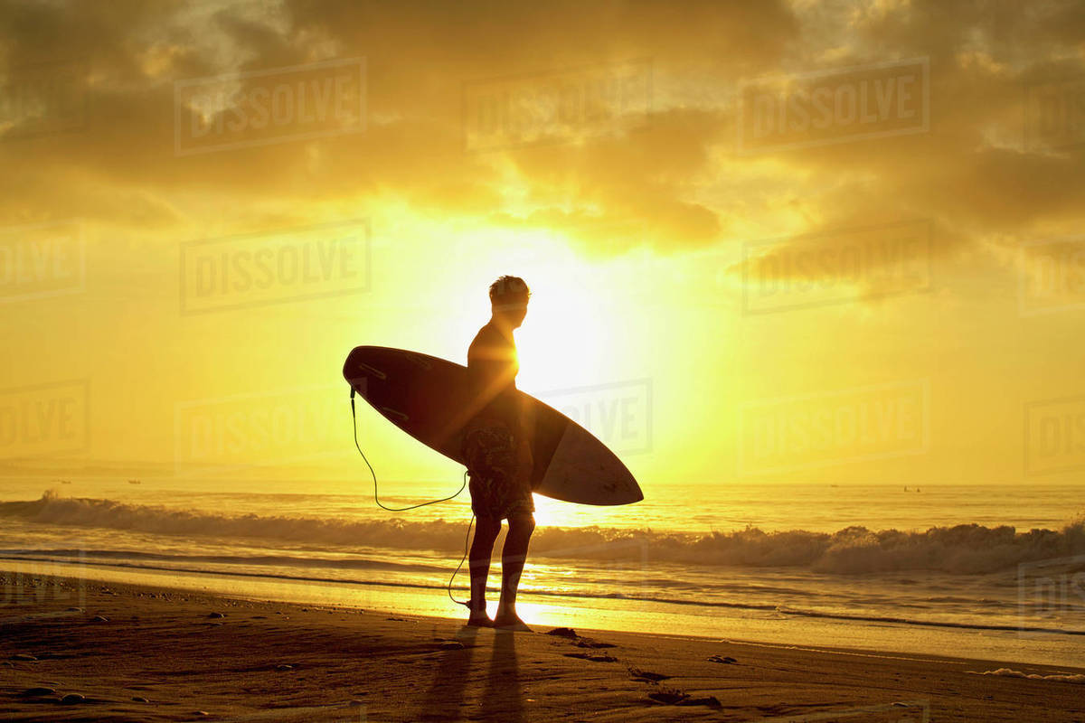 Silhouetted male surfer with surfboard on tranquil, sunset ocean beach Royalty-free stock photo