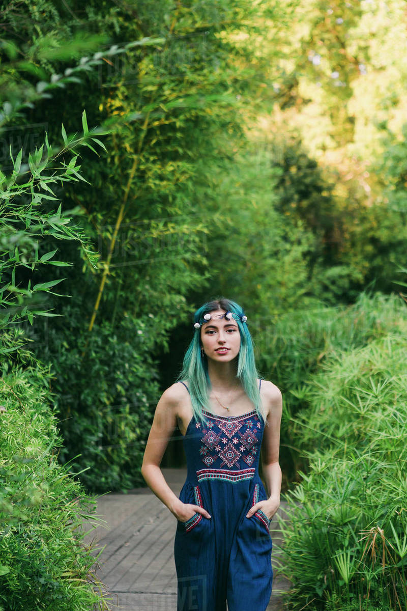 Portrait young woman with blue hair on footpath in lush park Royalty-free stock photo