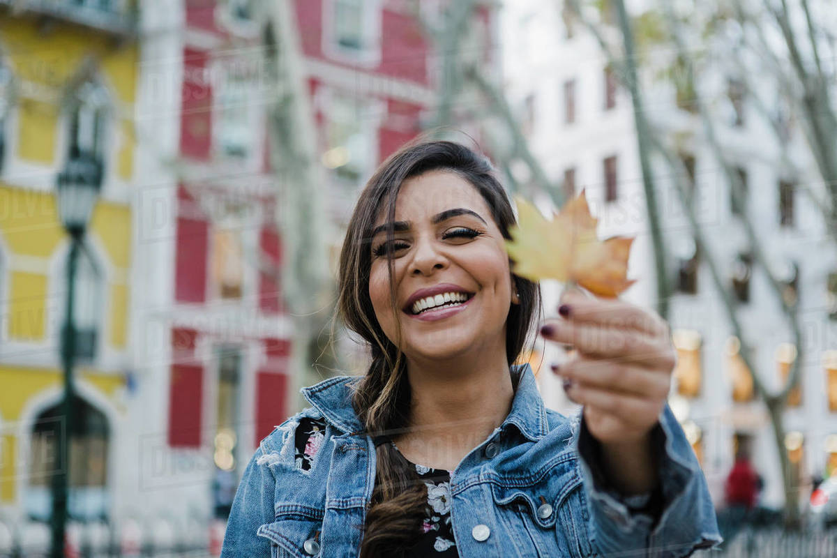 Portrait happy, playful young woman holding autumn leaf on urban street Royalty-free stock photo