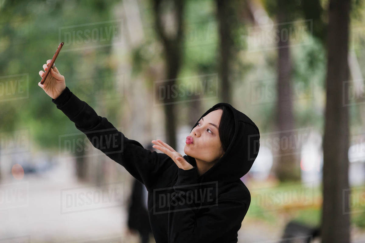 Confident, playful woman taking selfie with camera phone, blowing a kiss Royalty-free stock photo