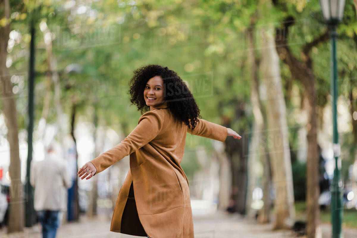 Portrait carefree young woman dancing on treelined sidewalk Royalty-free stock photo